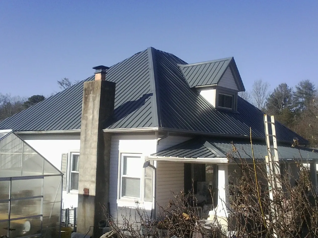 Dark blue standing seam metal roof on a white farmhouse with dormer — Slate & Tile Roof Repair by Roofing Brothers in East Sparta