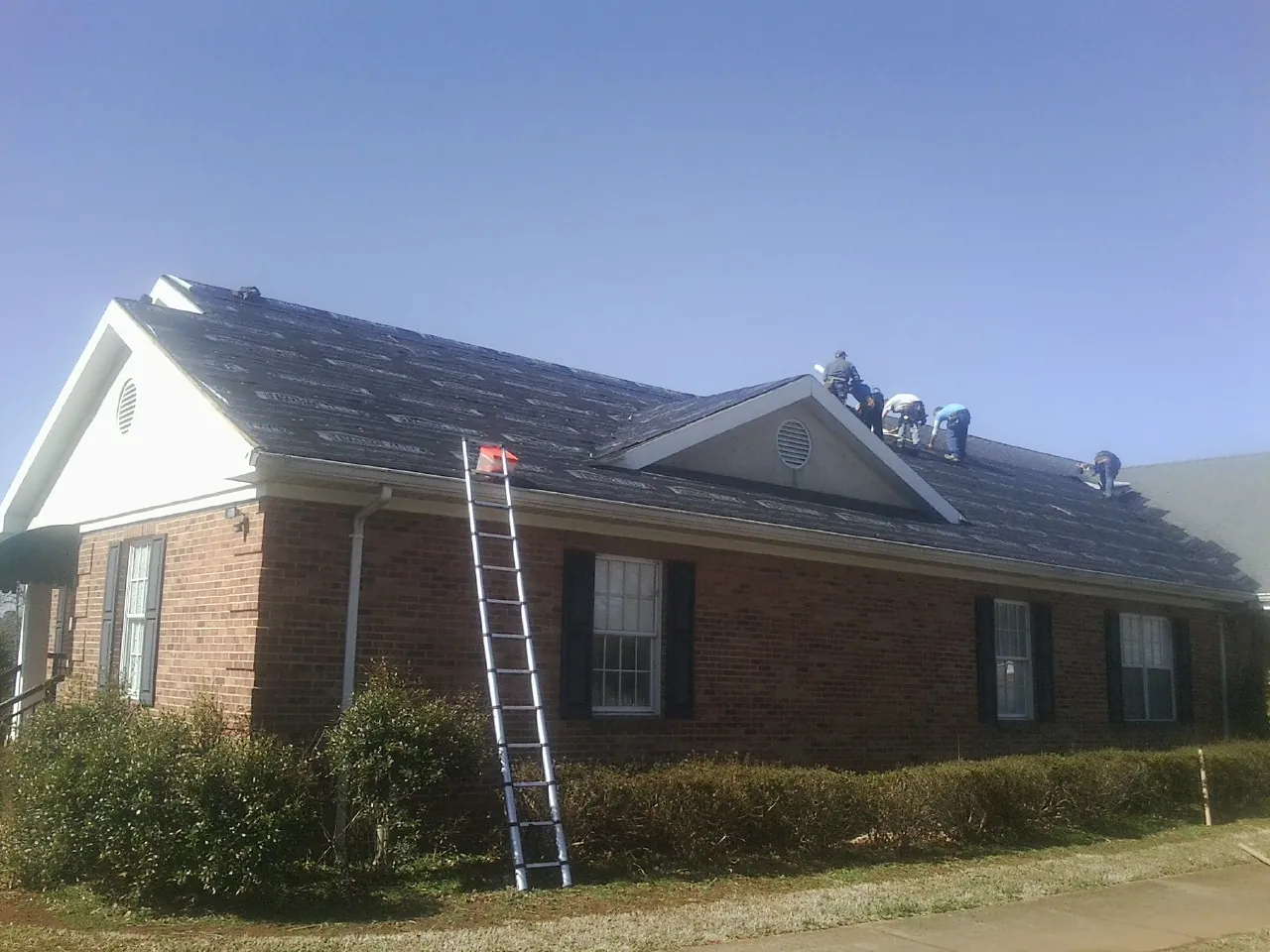 Crew tearing shingles off a brick ranch roof with a ladder set — Metal Roof Repair work by our crew in East Sparta