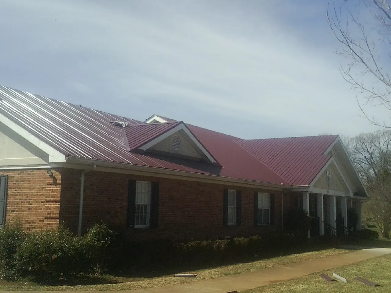 Red metal roof with gabled entries on a long brick building, from a Hail Damage Roof Repair job in East Sparta