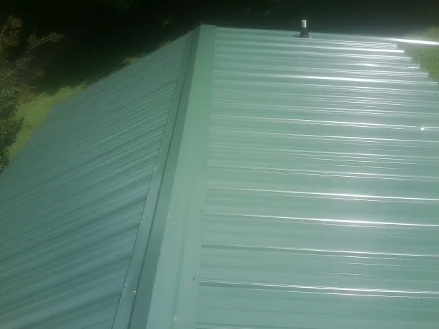 New green metal panels meeting at the ridge of a roof — Flat Roof Repair work by our crew in East Sparta