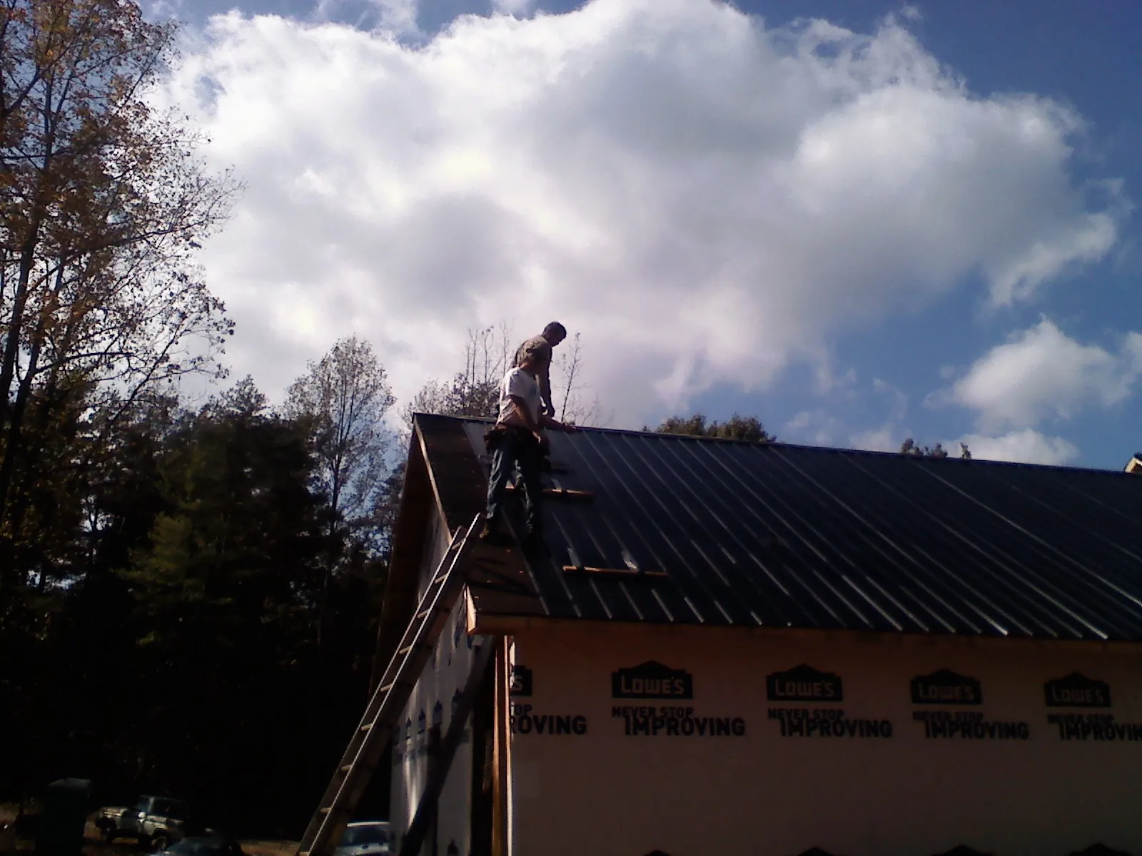 Roofer fastening dark metal panels high against a cloudy sky, from a Roof Inspection job in East Sparta
