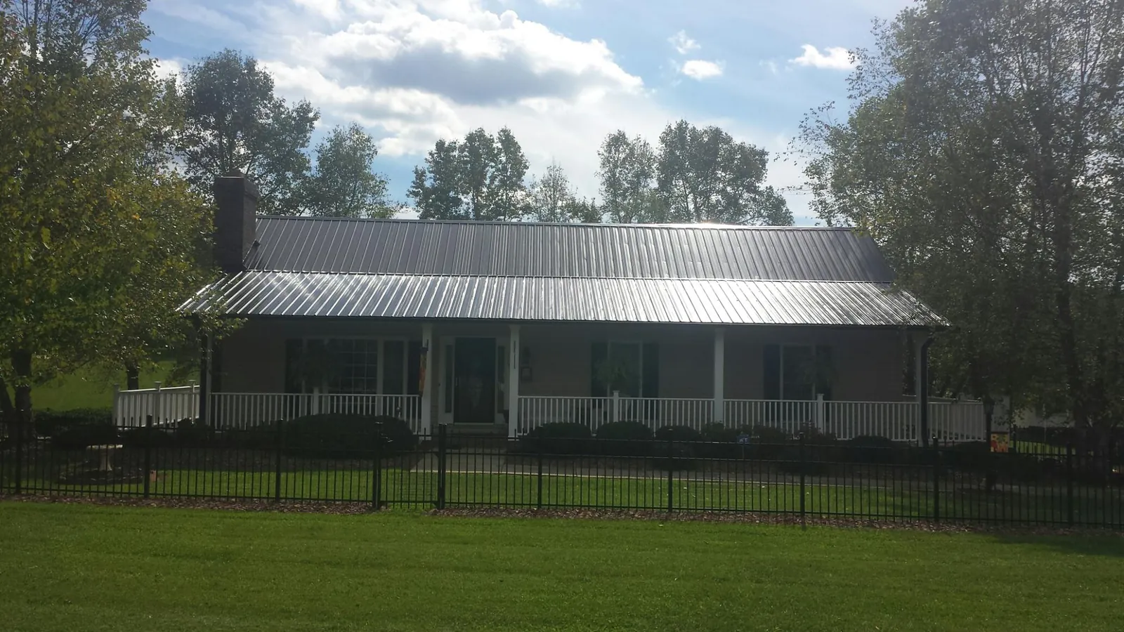 Gray metal roof on a brick ranch with a full width front porch — Gutter Guard Installation work by our crew in East Sparta