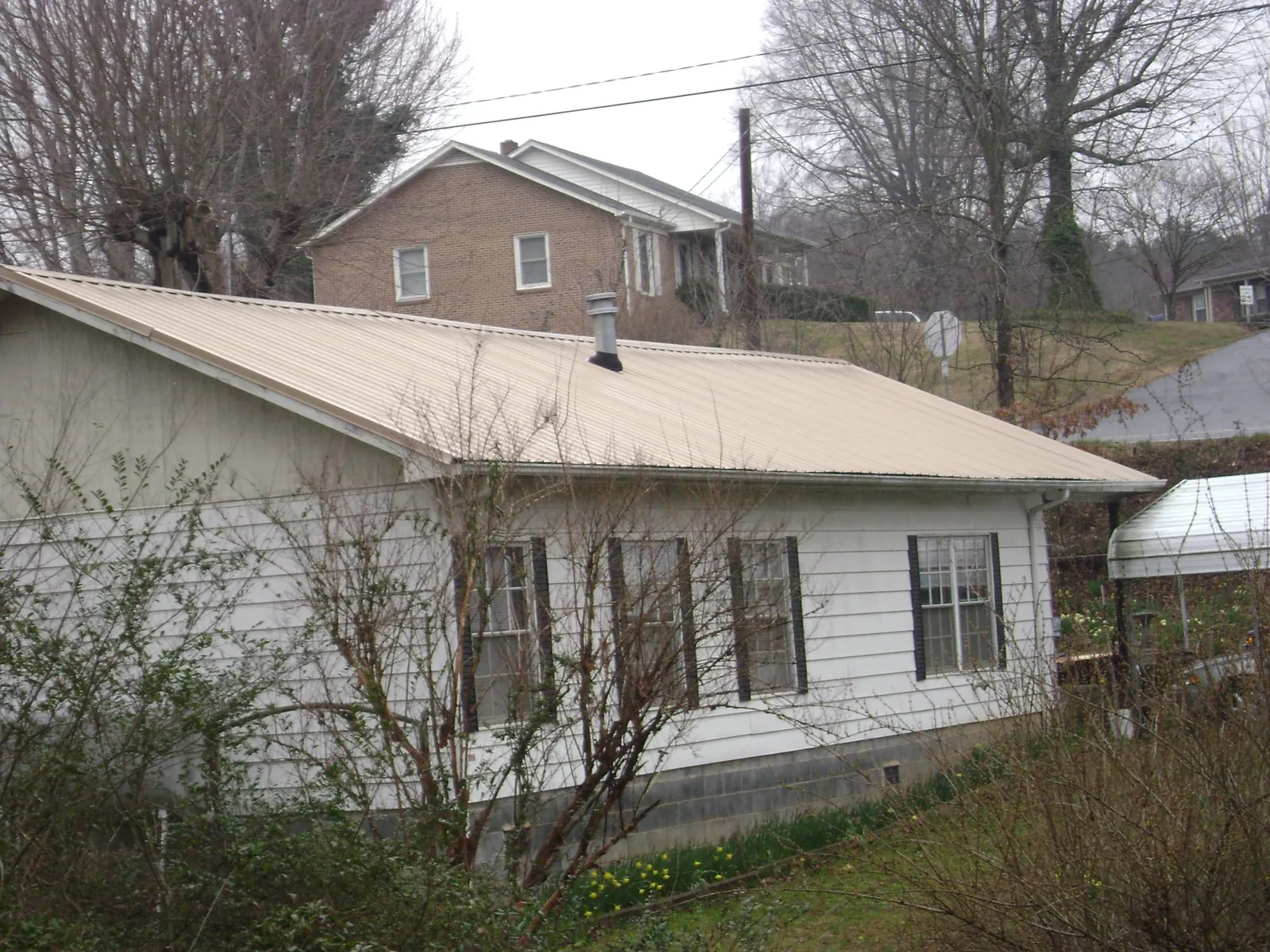 Tan metal roof on a white sided house set into a hillside — Commercial Roofing by Roofing Brothers in East Sparta