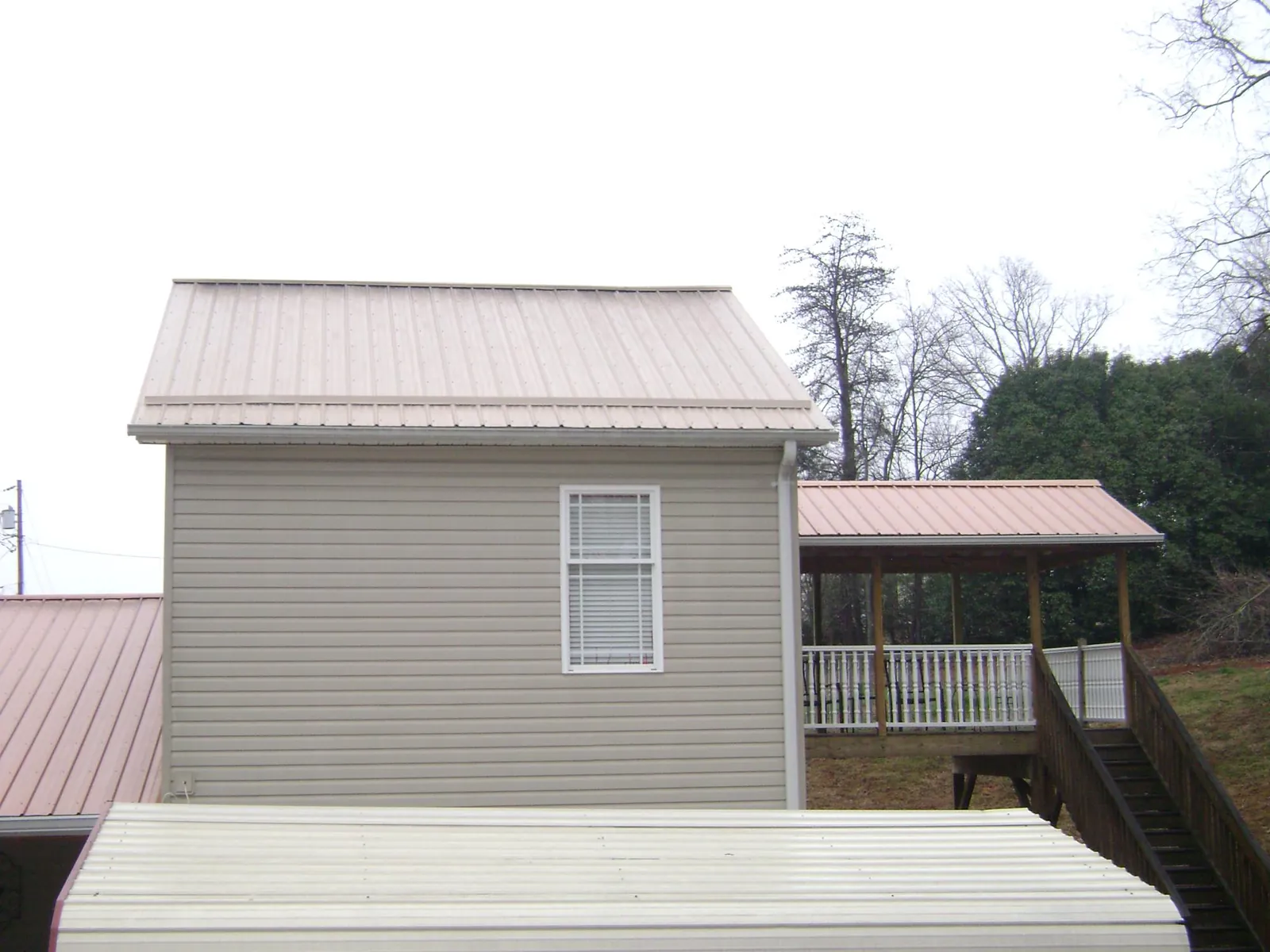 Tan metal roofs on a two story addition and attached porch, from a Roof Replacement job in East Sparta